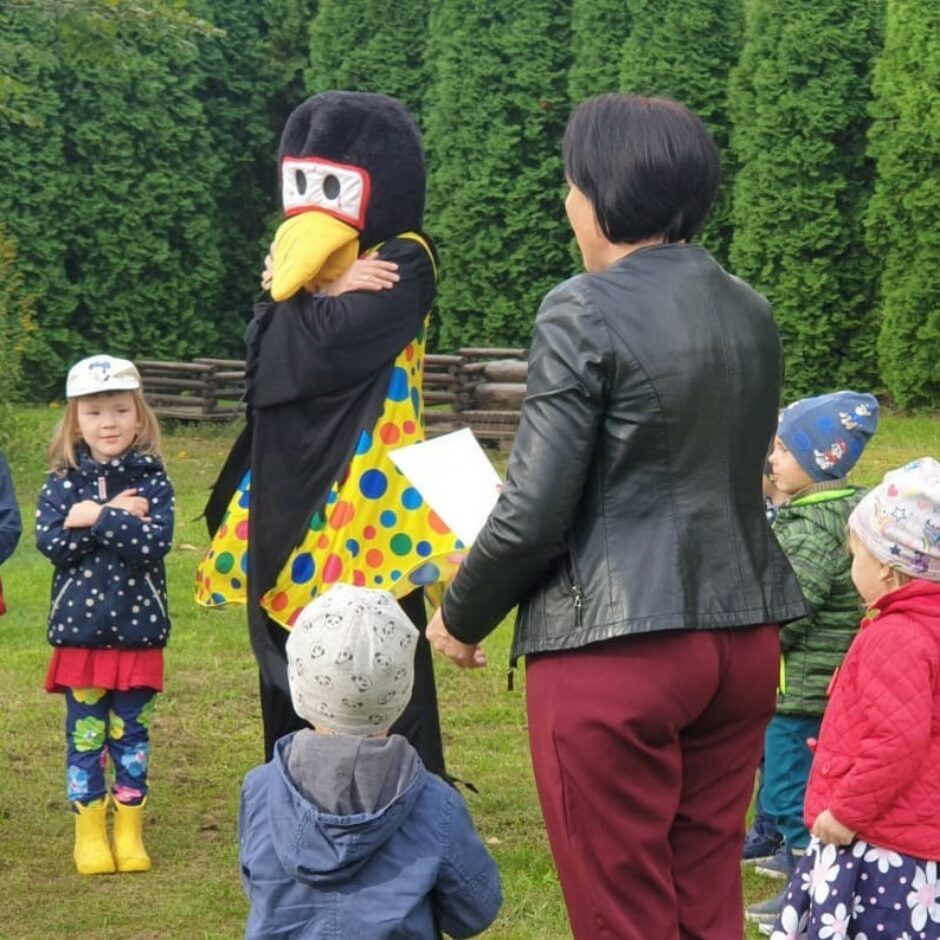 Pirmsskolas bērni āra laukumā kopā ar grupas skolotāju un maskā tērptu 
