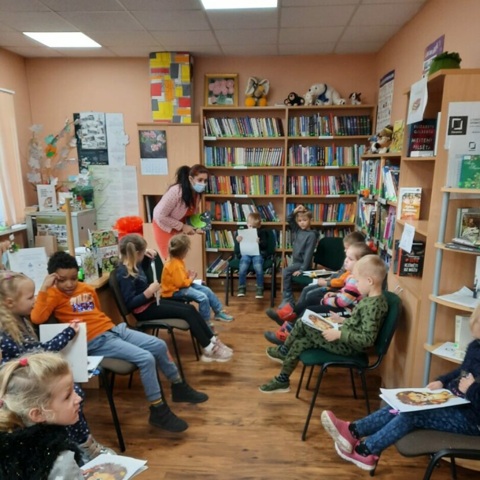 Bērni sēž bibliotēkā uz krēsliem.