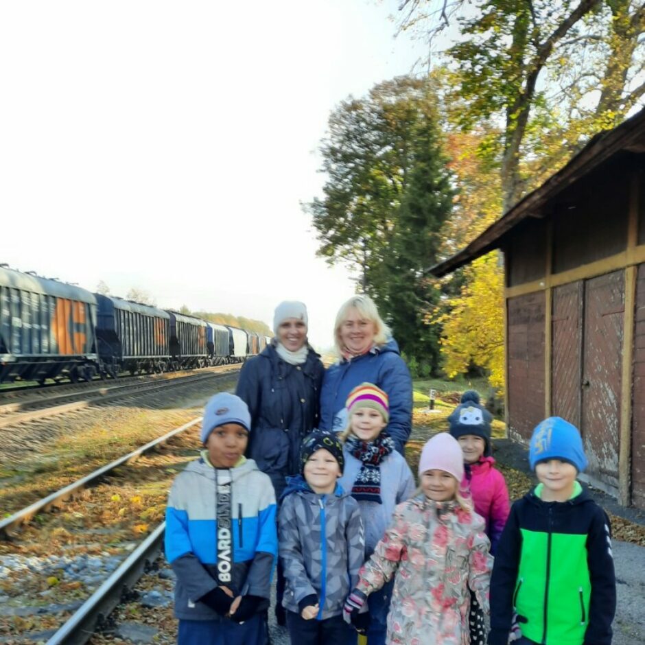 Bērni un skolotājas pie dzelzceļa sliedēm un kravas vilciena.