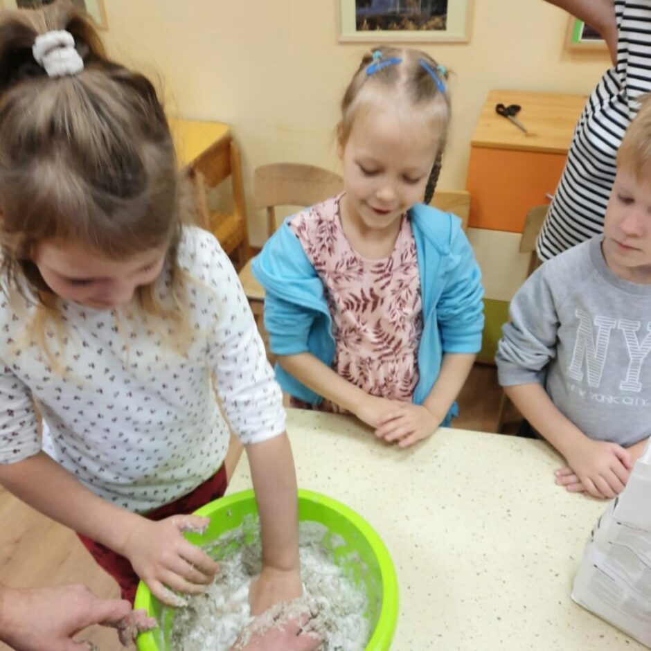 Meitene mīca mīklu, citi bērni vēro.