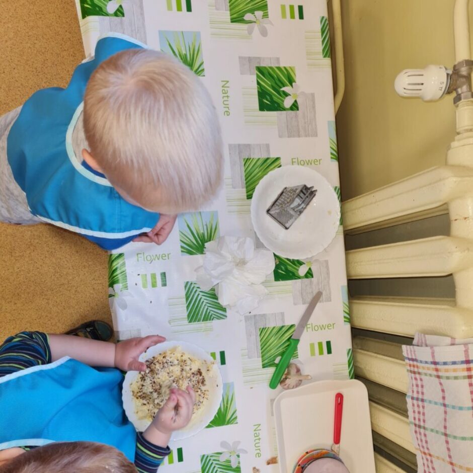 Viens bērns iemaisa sviestā sēkliņas, otrs bērns blakus vēro.