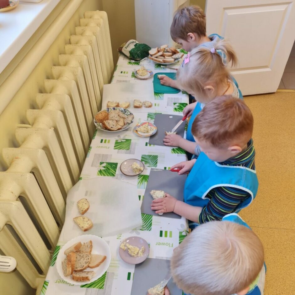 Četri bērni smērē uz maizītēm sviestu.