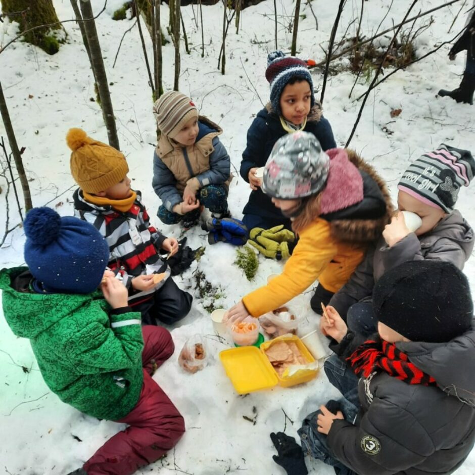 Bērni mežā dzer tēju un ēd uzkodas.