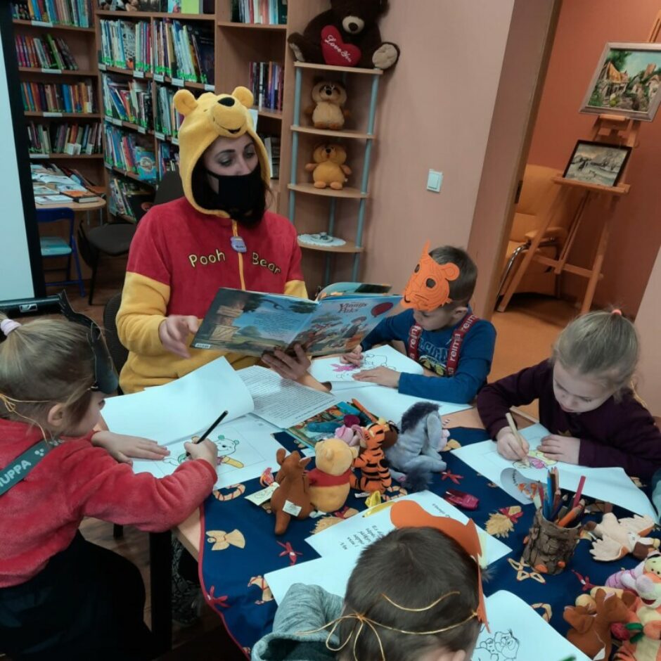 Bērni bibliotēkā klausās pasaku par Vinniju Pūku un krāso pasakas tēlus.