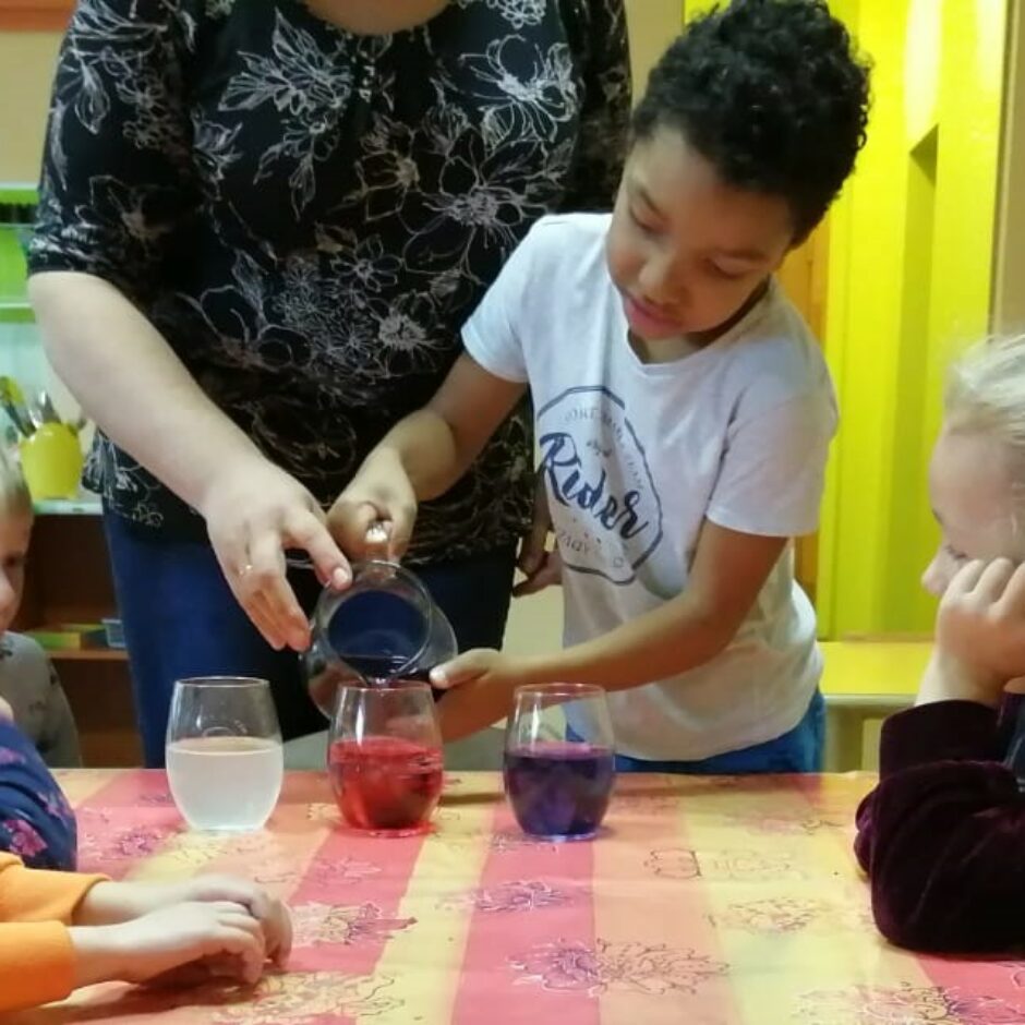 Bērni veic eksperimentu ar citronskābi, sodu un iekrāsotu ūdeni.