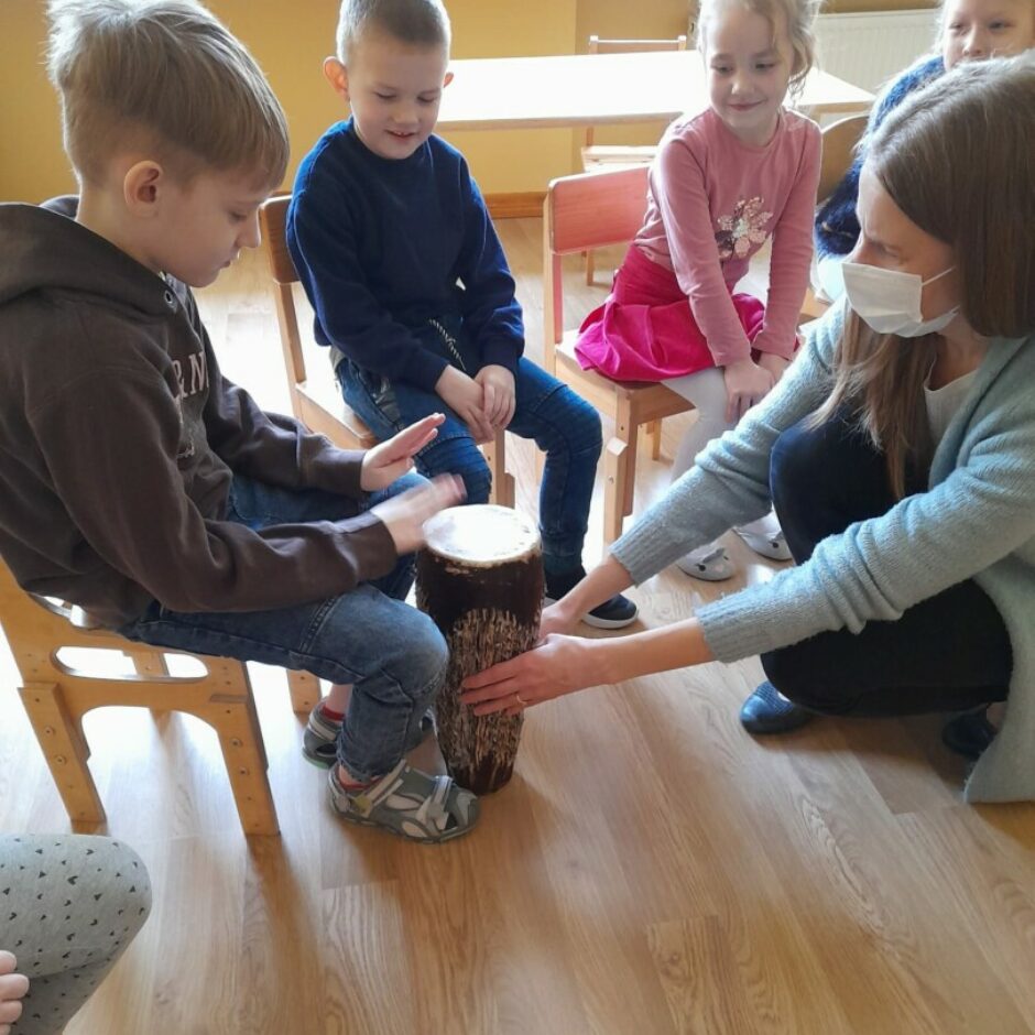 Zēns izmēģina spēlēt Āfrikas bungas. Citi bērni vēro.