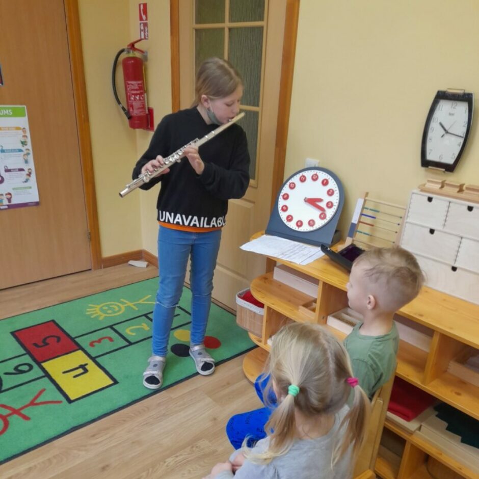 Skolniece grupas bērniem spēlē flautu.