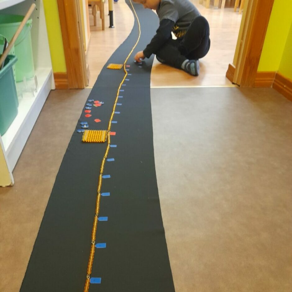 Zēns uz grīdas darbojas ar Montesori skaitīšanas materiālu.