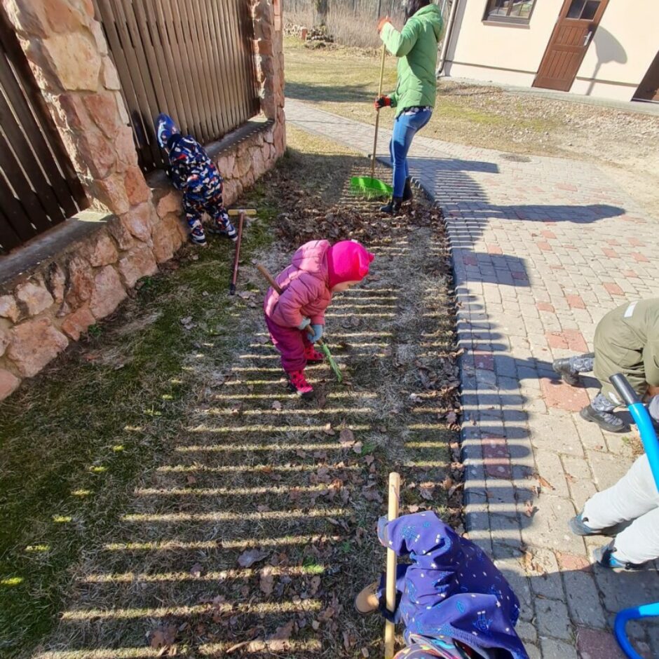 Bērni ar skolotāju sakopj apkārtni - grābj lapas.