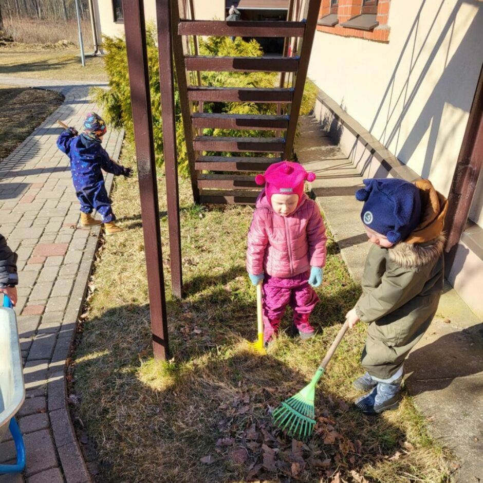 Bērni sakopj apkārtni - grābj lapas.