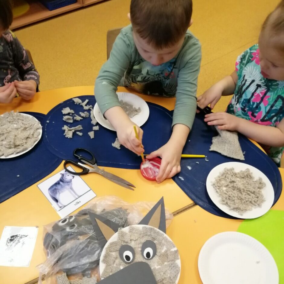 Bērni darbojas pie galda - griež audumu un strādā ar līmi un otu.