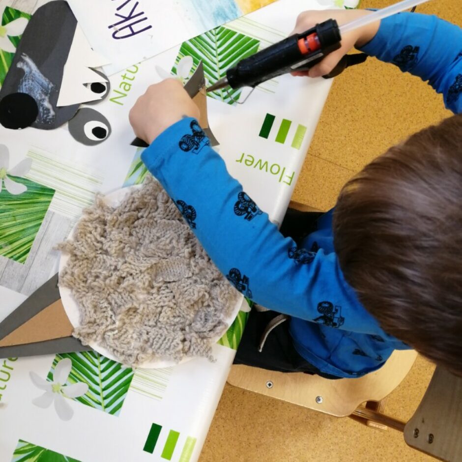 Bērns pie galda darbojas ar līmes pistoli.