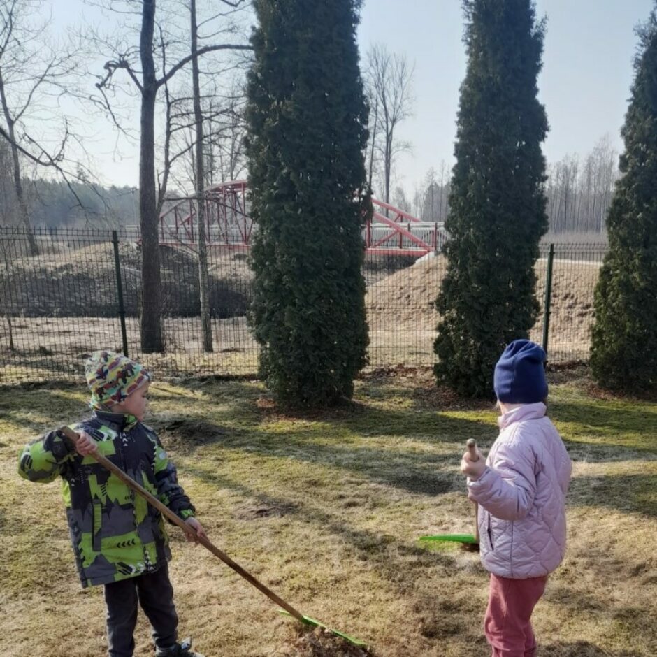Meitene un zēns grābj āra laukumiņu.