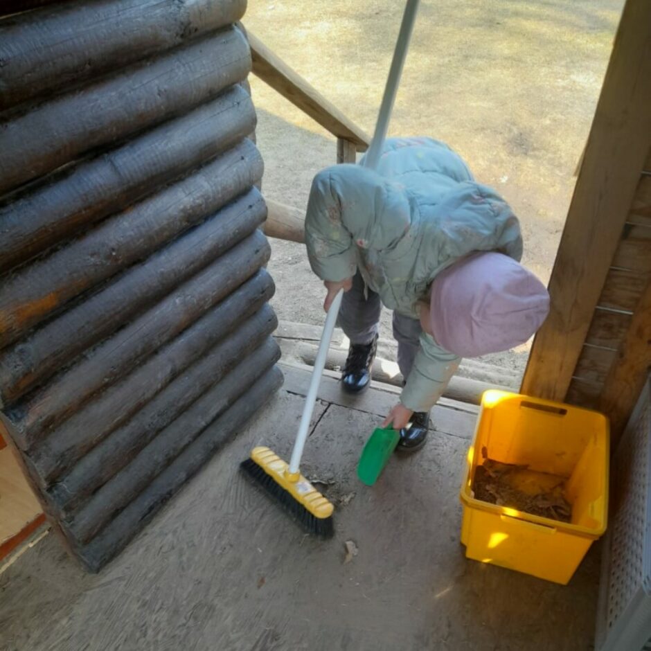 Meitene āra rotaļu namiņā slauka grīdu.