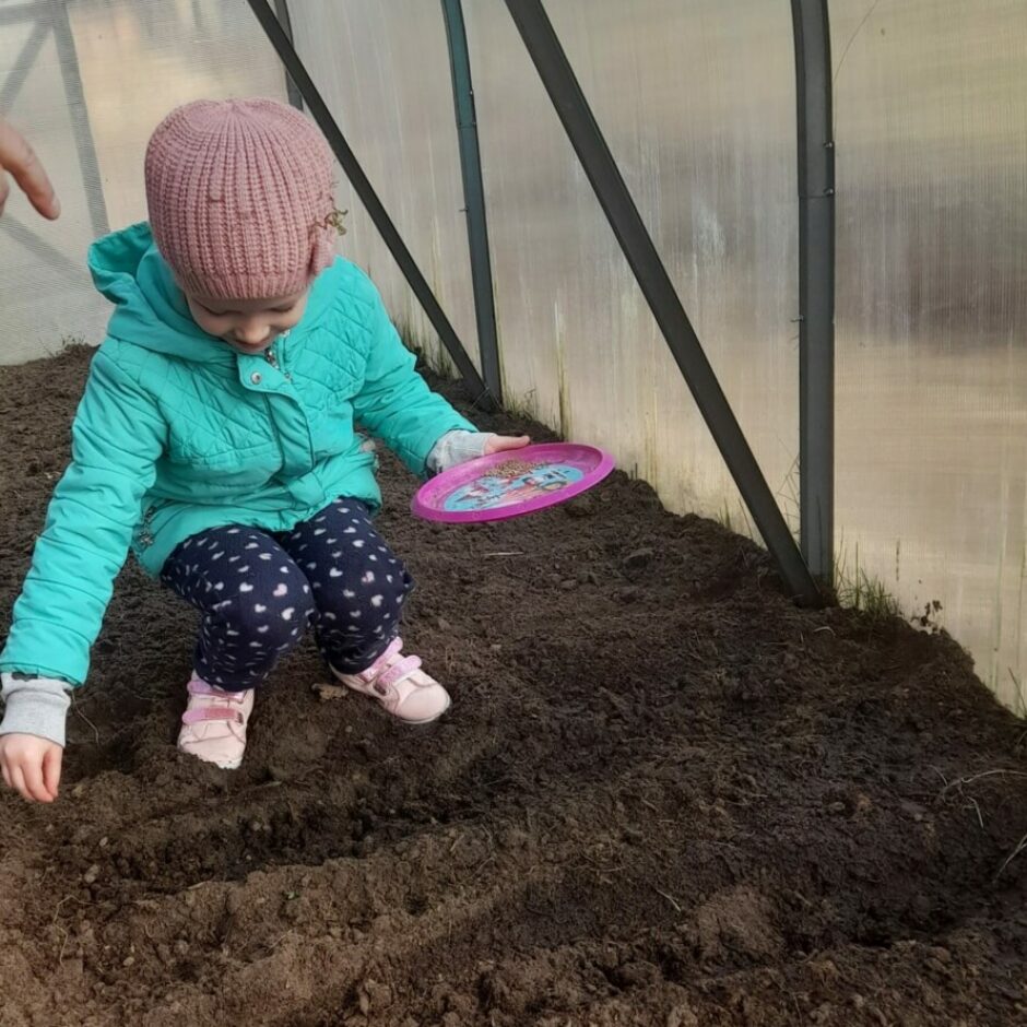 Meitene siltumnīcā, vadziņās sēj sēkliņas.