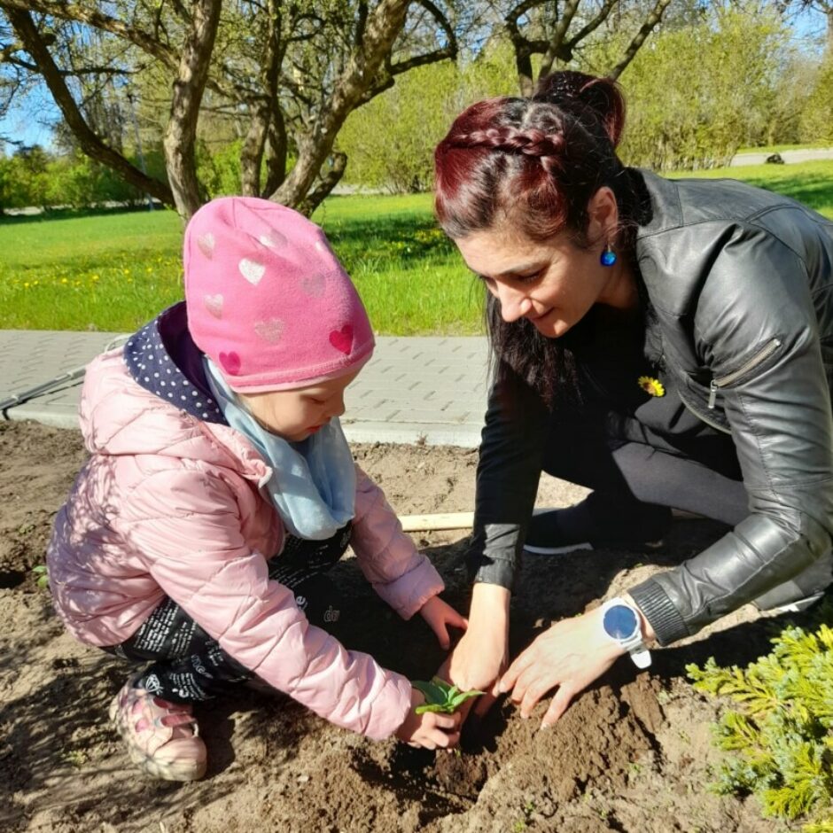Meitene ar biblotekāres palīdzību stāda saulespuķi.