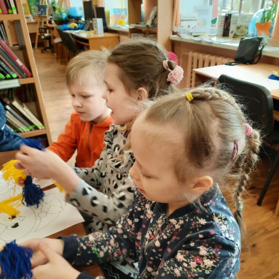 Bērni bibliotēkā no dzijas veido putniņus.