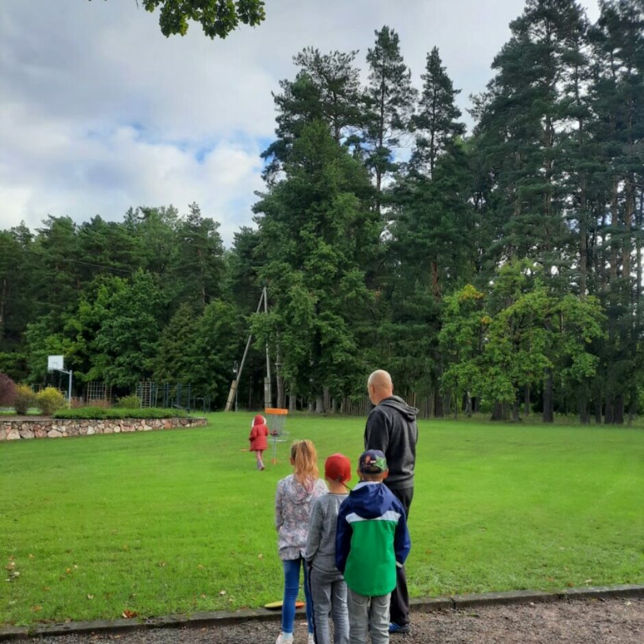 Skolotājs un 4 bērni laukā spēlē diskgolfu