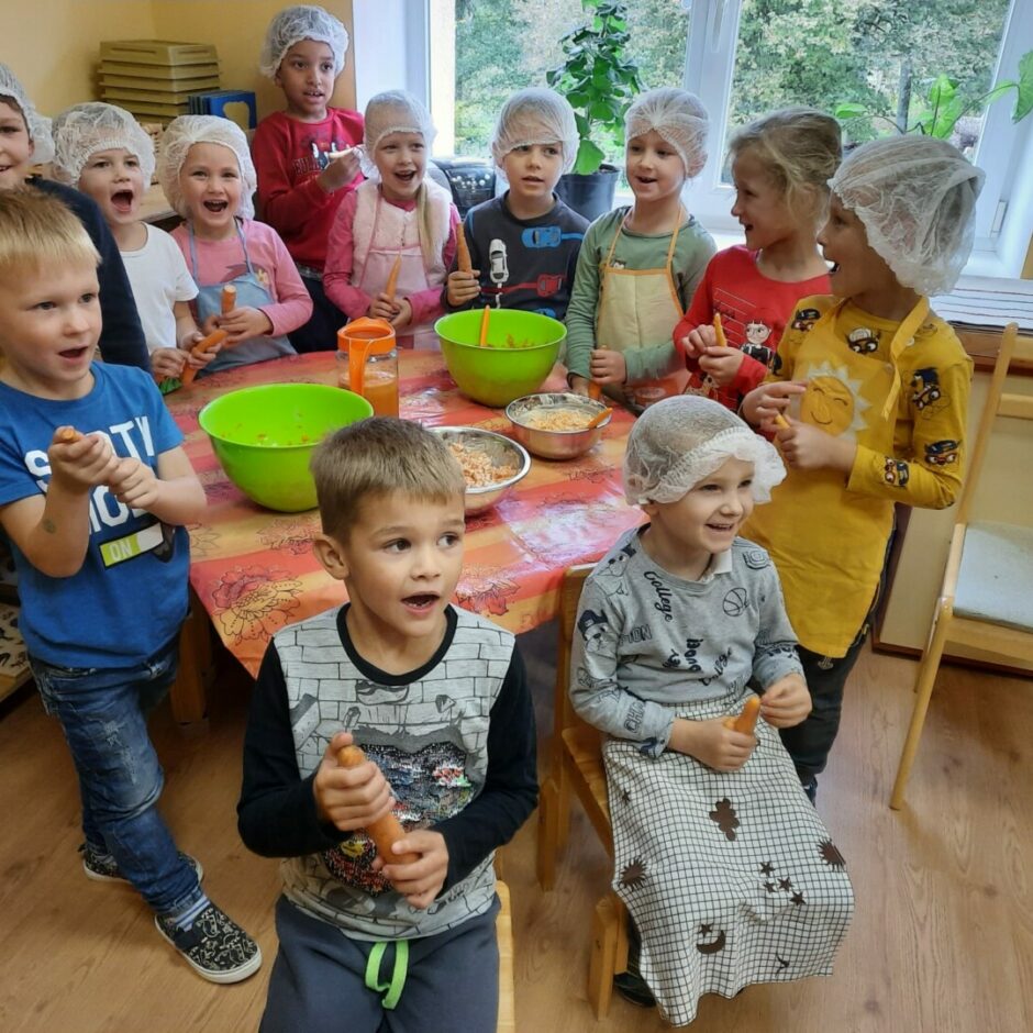 Priecīgi bērni pie galda, uz kura atrodas pagatavotie burkānu salāti.