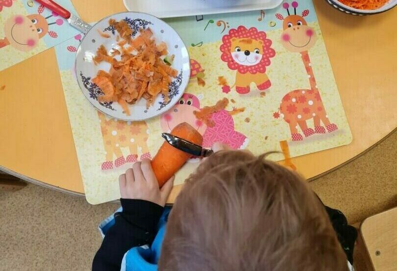 Bērns ar mizojamo nazi mizo burkānu.