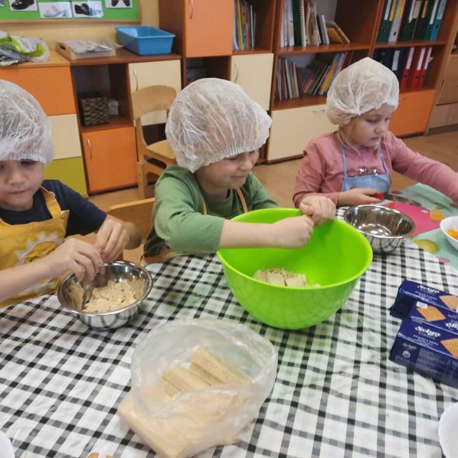 Bērni pie galda drupina cepumus un griež marmelādi saldajai ruletei.