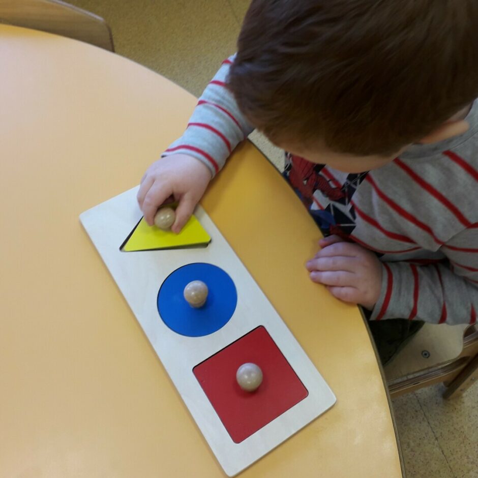 Zēns mācās satvert, izņemt un ielikt dažādas ģeometriskās figūras tām paredzētajās vietās.
