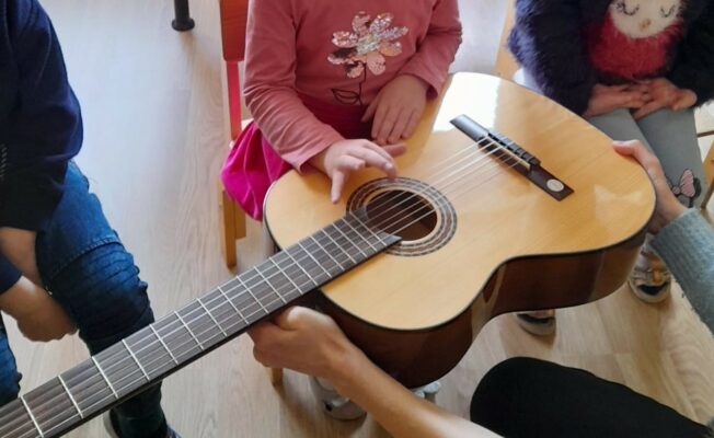 Meitene izmēģina spēlēt uz ģitāras stīgām.