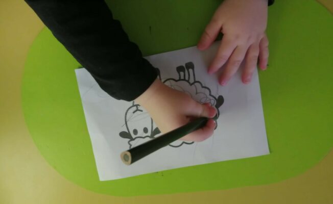Bērns darbojas ar zīmuli - zīmē uz lapas ar aitiņas siluetu.