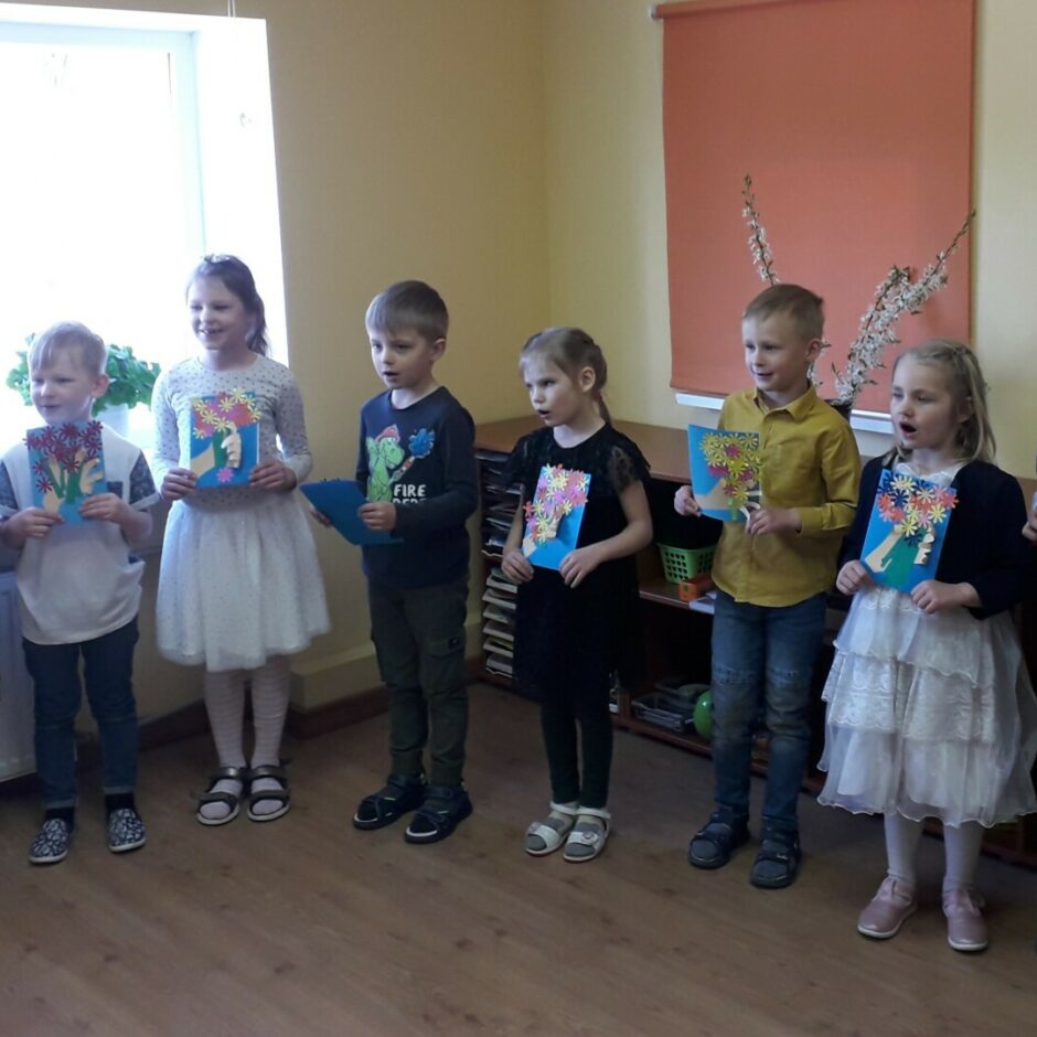 Bērni dzied dziesmu mammām ar apsveikumiem rokās.