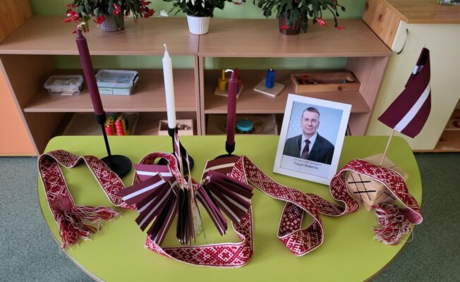 Uz galda tautiskā josta, sveces, Latvijas karodziņš un Latvijas prezidenta Foto.