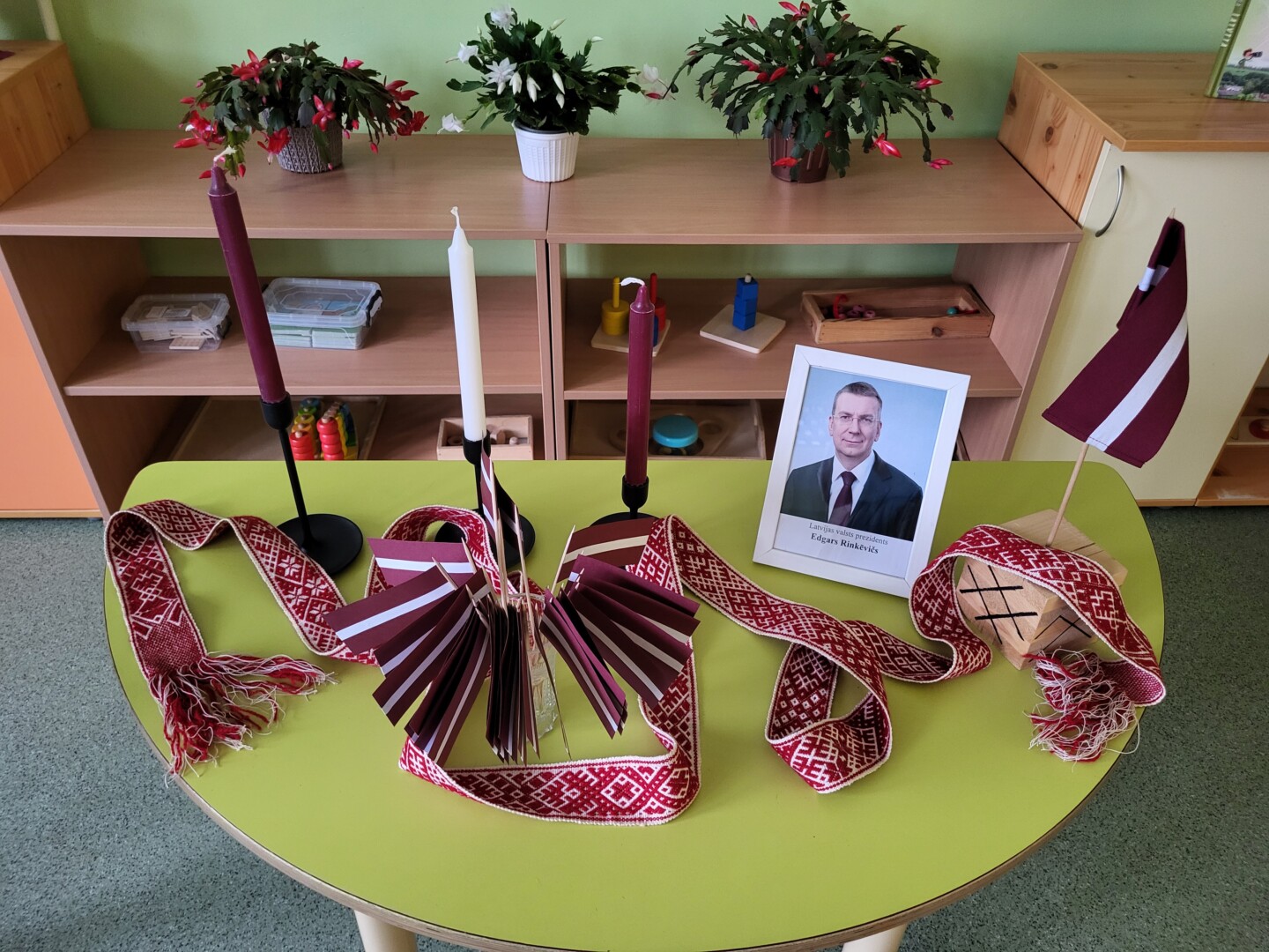 Uz galda tautiskā josta, sveces, Latvijas karodziņš un Latvijas prezidenta Foto.