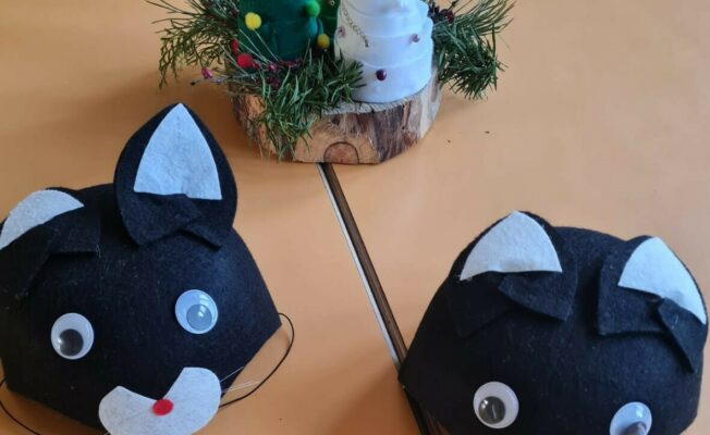 Uz galda divas kaķa maskas, dzijas eglīšu kompozīcija.