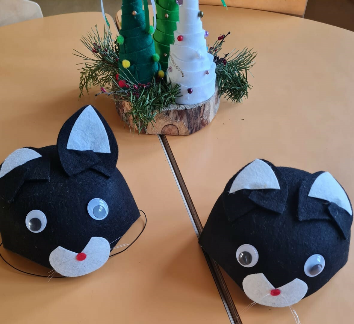 Uz galda divas kaķa maskas, dzijas eglīšu kompozīcija.