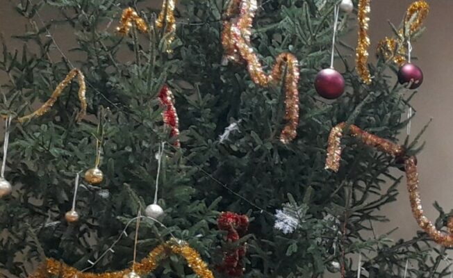Izrotāta liela Ziemassvētku egle ar spožām vītnēm un bumbuļiem.
