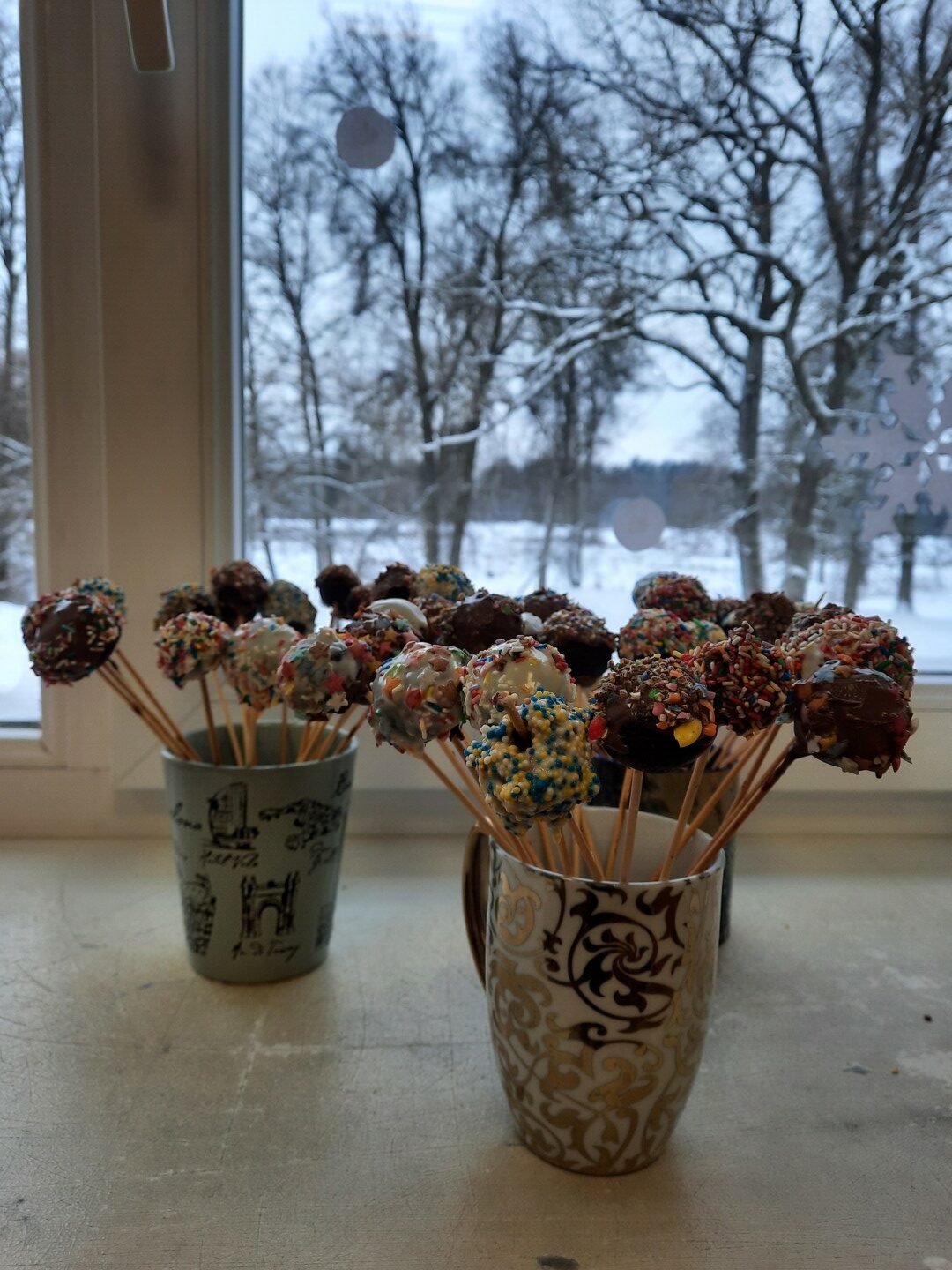 Šokolādes konfektes uz kociņa divās krūzēs.