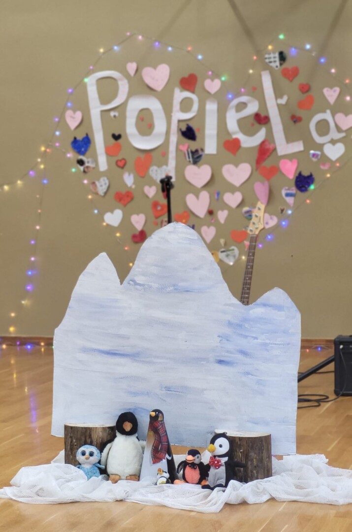 papīra sirsniņas pie sienas, uzraksts Popiela, dekorācijas - rotaļlietas pingvīni un kartona ledusgabals.