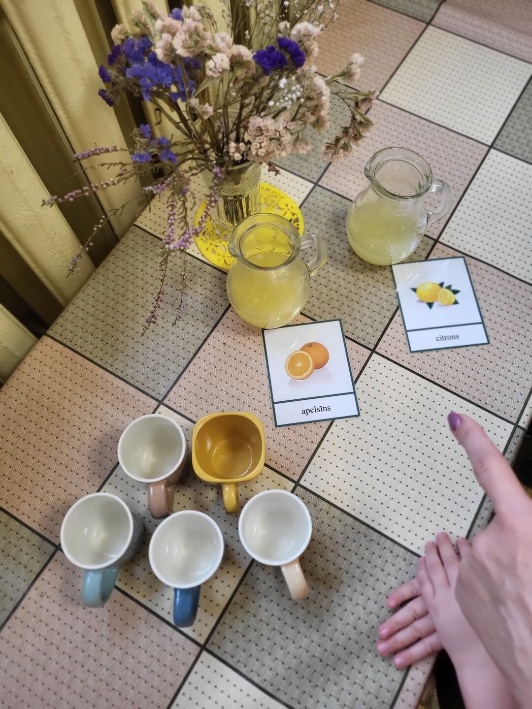 Krūzītes uz galda in divas stikla krūzes ar citronu un apelsīnu sulu