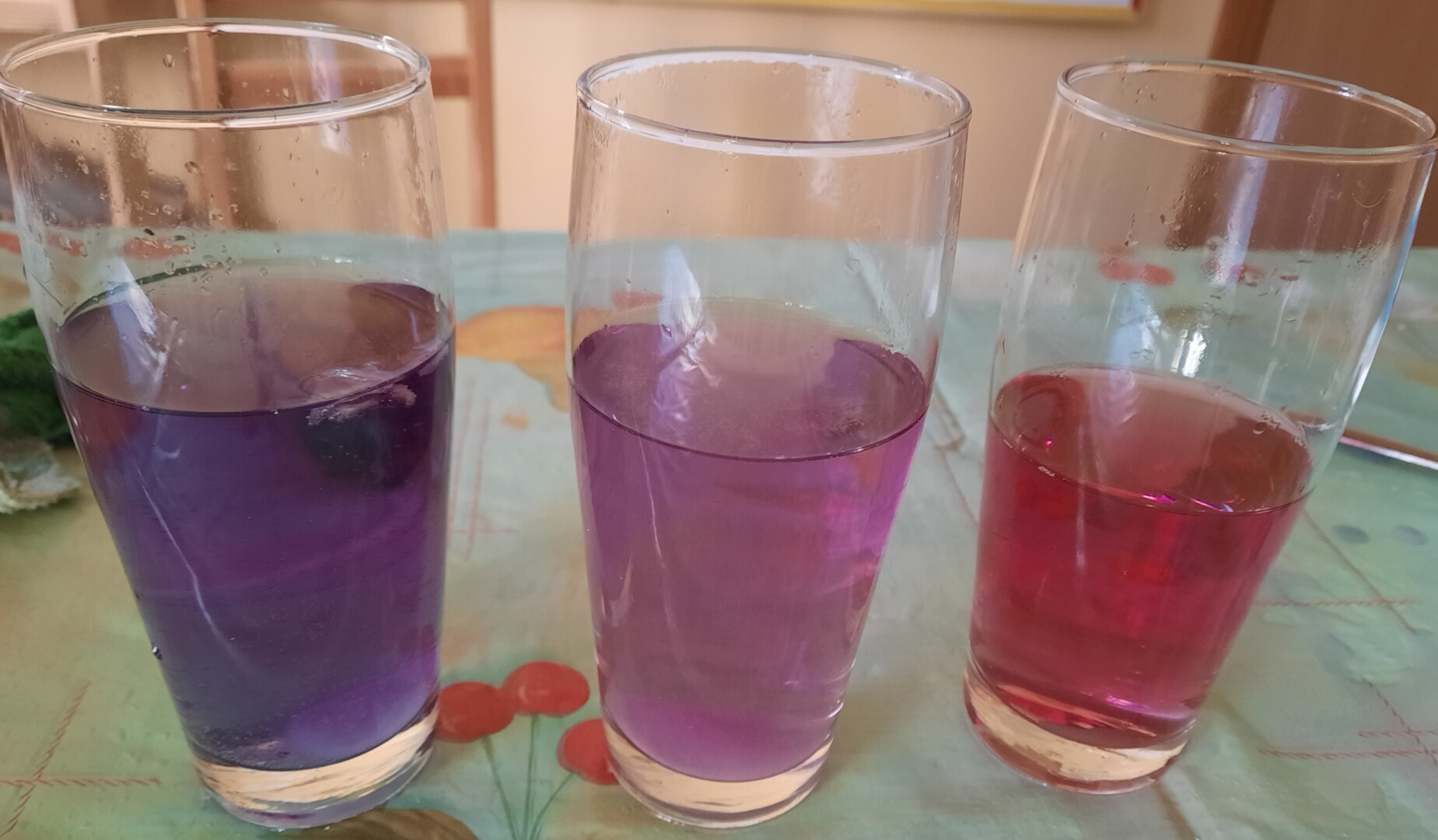 Trīs glāzes ar krāsainu ūdeni iekšā stāv uz galda