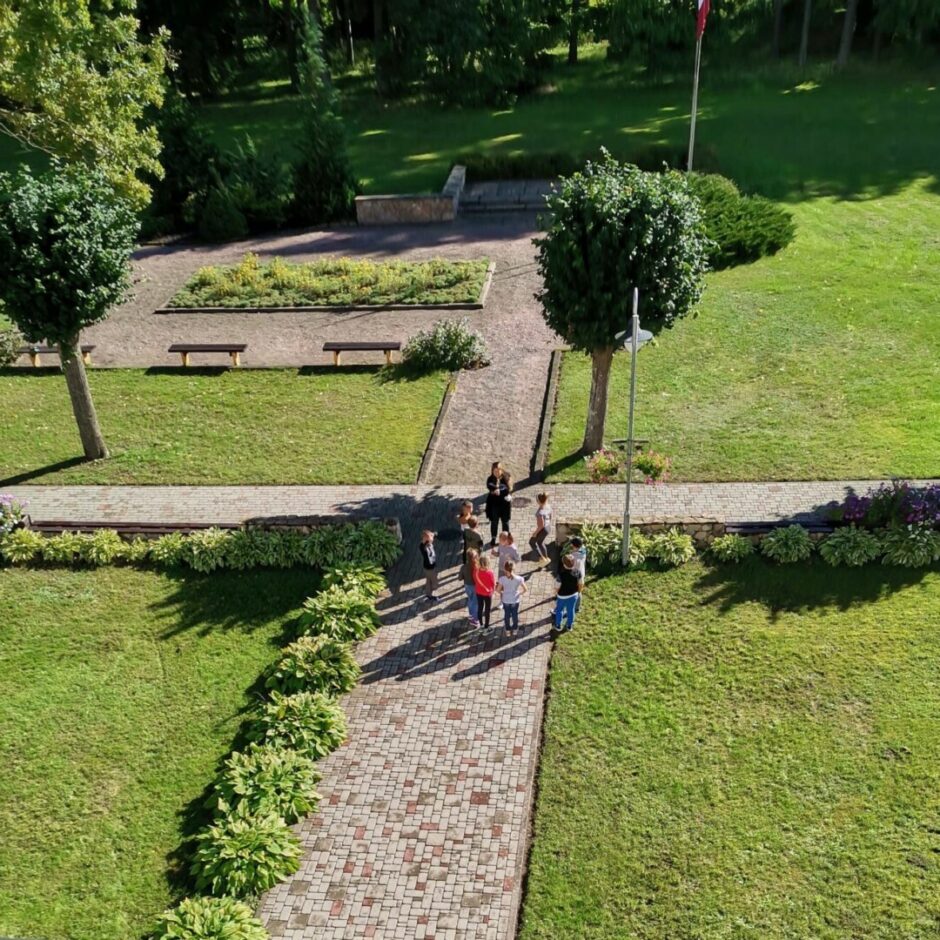 Skolotāja un 10 bērni spēlē spēli laukā - skats no augšas