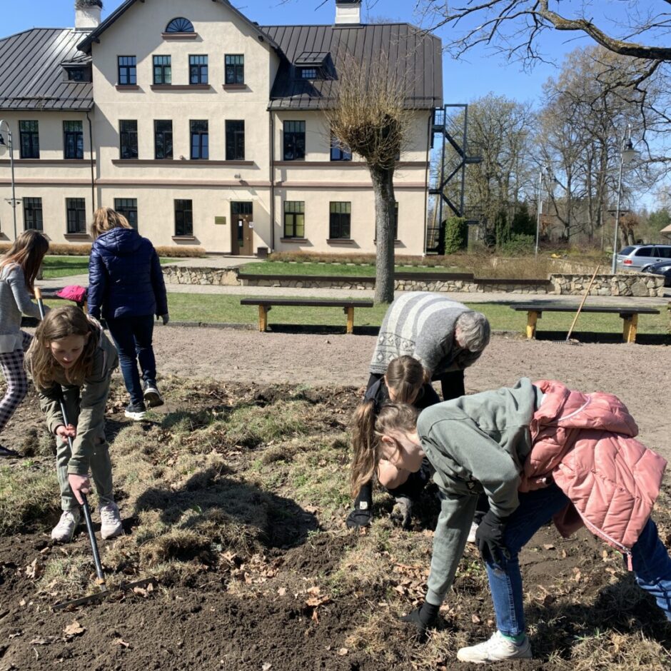 5 skolēni strādā dobē, rok puķes