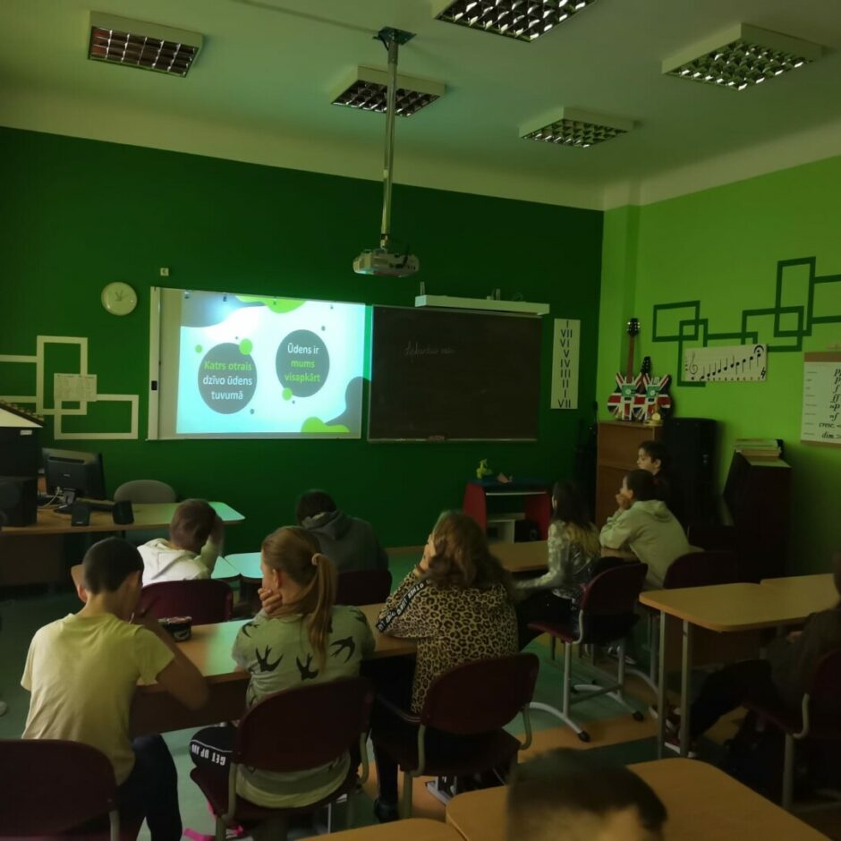 Skolēni skatās un klausās lekciju mūzikas kabinetā.