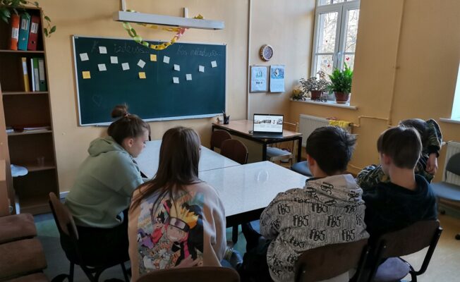 Skolēni sēž pie galda un skatās uz datoru